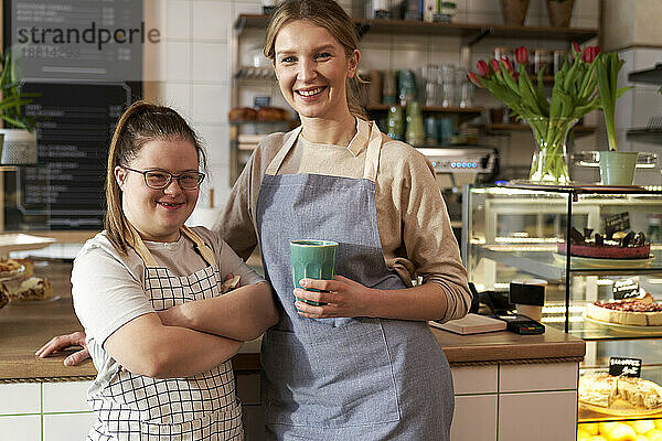 Happy cafe owner with down syndrome standing by colleague in coffee shop