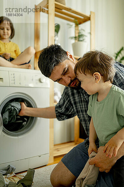 Father and son washing clothes in machine at home