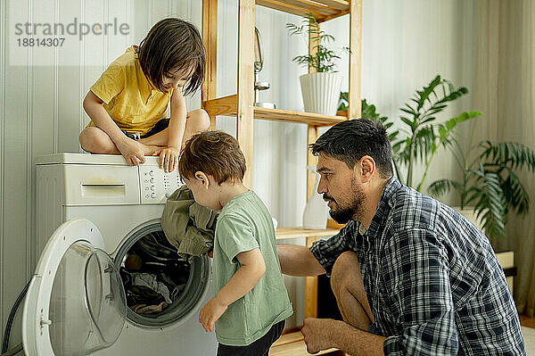 Vater mit Kindern hilft beim Wäschewaschen in der Maschine zu Hause
