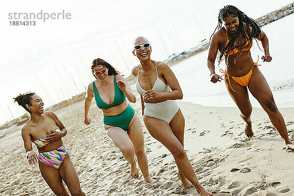 Fröhliche Freunde in Bikinis laufen am Strand im Sand