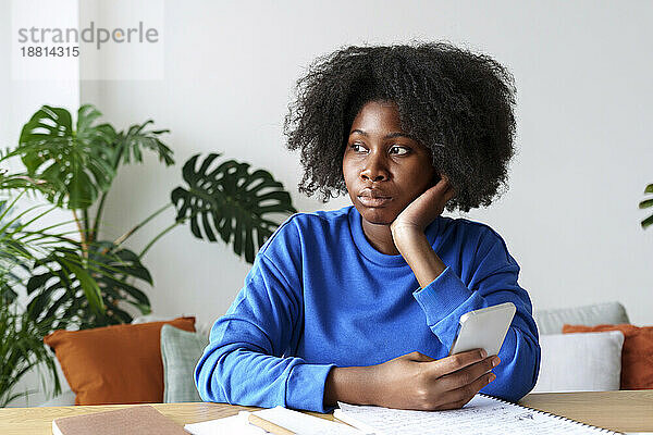 Nachdenkliche Afro-Frau mit Smartphone plant Hausfinanzen