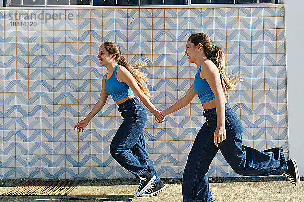 Sisters holding hands and running in front of wall