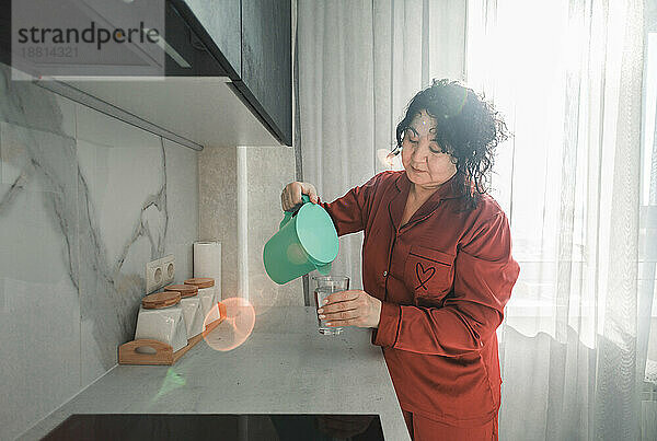 Reife Frau gießt zu Hause Wasser in ein Glas
