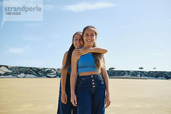Glückliche Schwestern stehen an einem sonnigen Tag im Skateboardpark zusammen