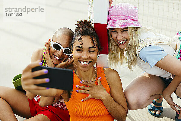 Smiling woman taking selfie through mobile phone with friends