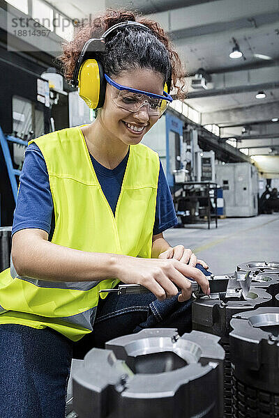 Lächelnder Ingenieur in reflektierender Kleidung  der in einer modernen Fabrik arbeitet