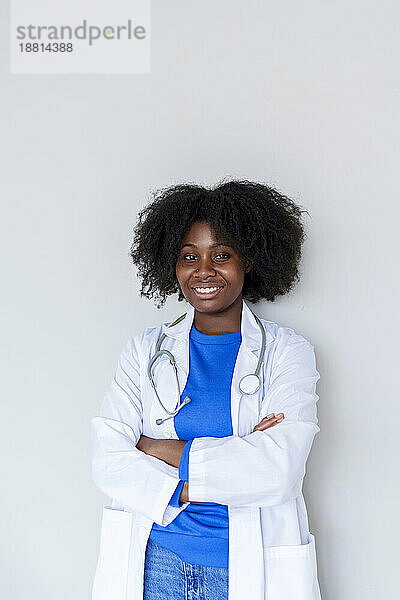 Junger Afro-Arzt mit verschränkten Armen steht vor weißem Hintergrund
