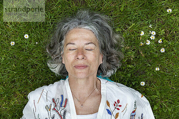 Ältere Frau mit geschlossenen Augen liegt auf grünem Gras