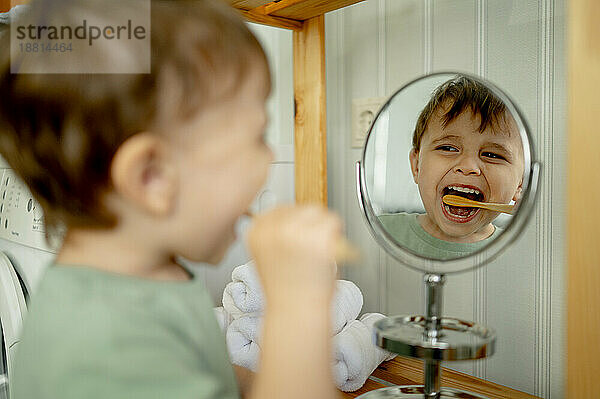 Boy brushing teeth looking in mirror at home