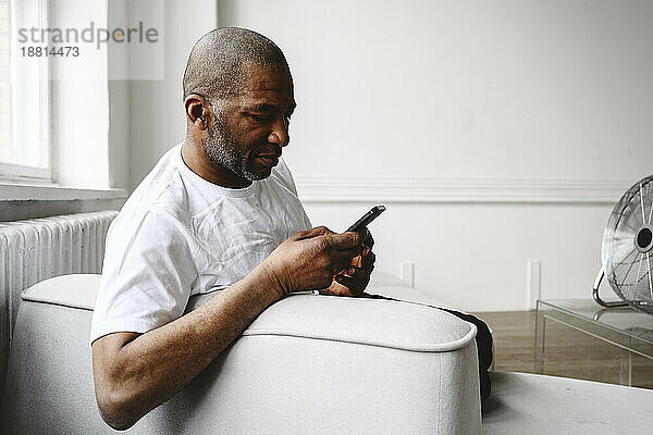 Reifer Mann benutzt Smartphone auf Sofa zu Hause
