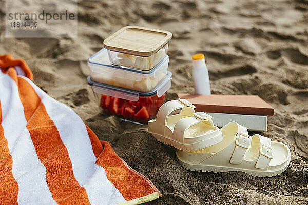 Sandals and fruit containers with towel on sand at beach