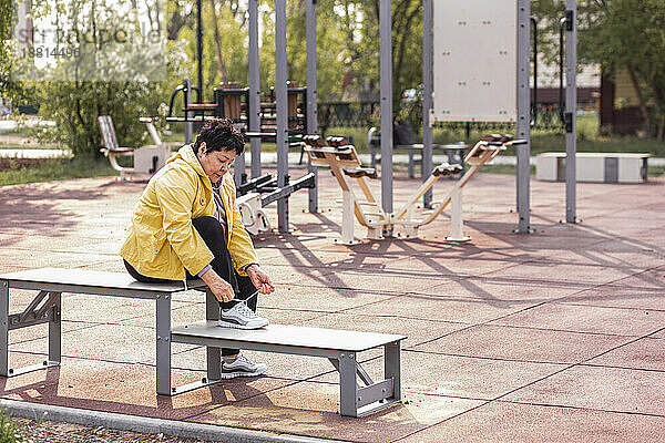 Ältere Frau bindet Schnürsenkel  sitzt auf Bank im Park