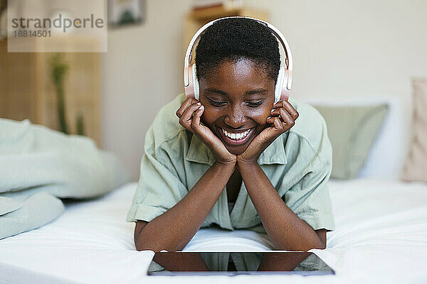 Glückliche junge Frau  die zu Hause im Bett einen Tablet-PC benutzt