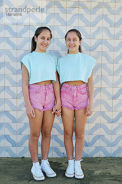 Happy twin sisters standing together in front of patterned wall