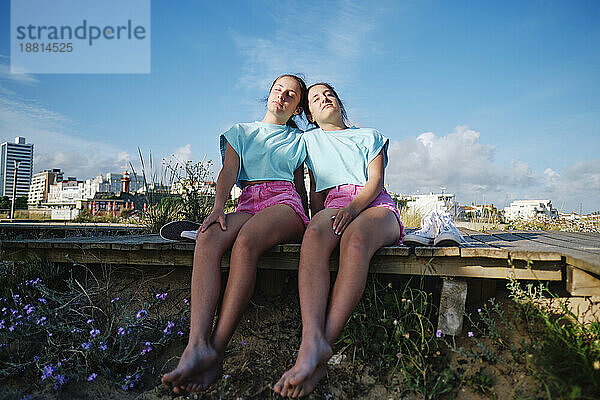 Zwillingsschwestern tragen passende Outfits und entspannen sich auf dem Steg am Strand