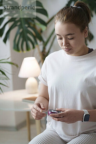 Frau  die zu Hause sitzt und ein digitales Glukometer verwendet