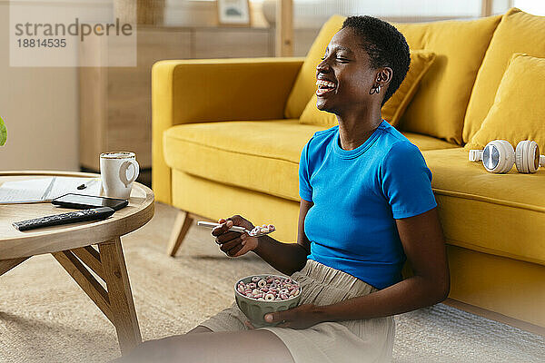 Cheerful young woman eating cereals and watching TV at home