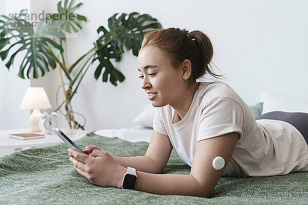 Frau mit Diabetes benutzt Smartphone  liegt zu Hause im Bett