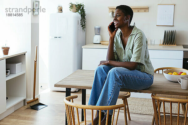 Glückliche junge Frau  die zu Hause in der Küche mit dem Smartphone spricht