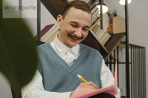 Smiling man with moustache taking notes sitting in studio