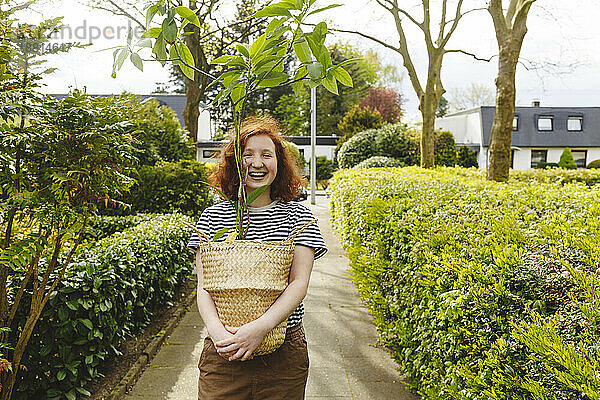 Glückliches Mädchen steht mit Avocadopflanze auf Fußweg