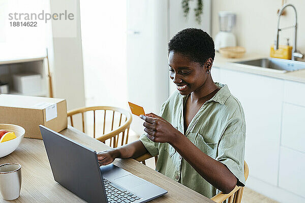 Glückliche Frau  die zu Hause per Kreditkarte auf dem Laptop bezahlt
