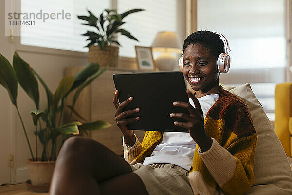 Glückliche junge Frau mit kabellosen Kopfhörern  die sich zu Hause einen Film auf einem Tablet-PC ansieht