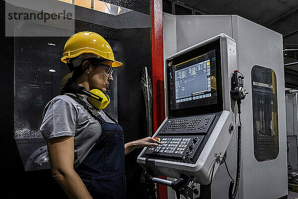 Ingenieur trägt Schutzhelm und bedient die CNC-Maschinentastatur in einer modernen Fabrik