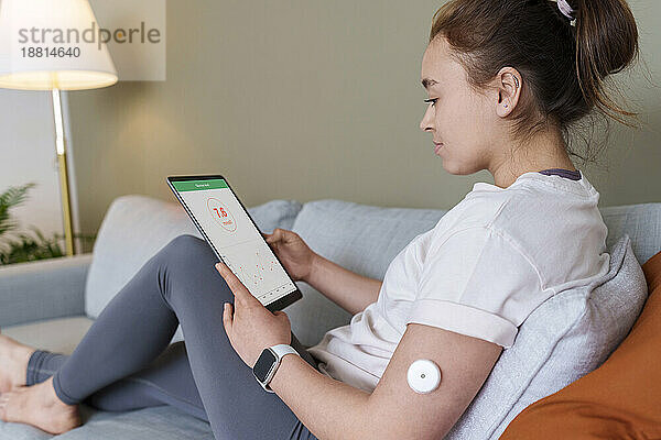 Frau benutzt zu Hause einen Tablet-PC mit Diabetes-Glukosesensor am Arm