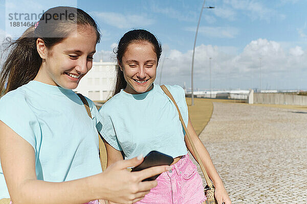 Glückliche Zwillingsschwestern  die an einem sonnigen Tag ihr Smartphone nutzen