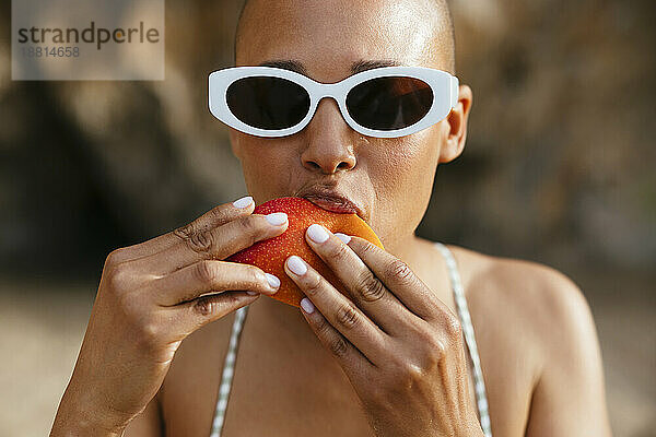 Frau mit Sonnenbrille isst Mango am Strand