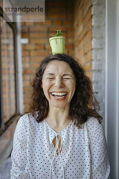 Cheerful woman standing with potted plant on head