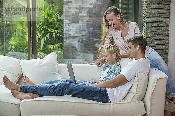 Glücklicher Mann und Frau mit Sohn  die zu Hause Laptop benutzen
