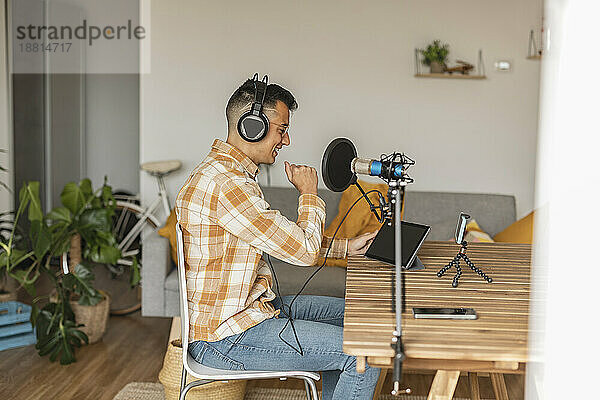 Mann Podcasting vor Smartphone und Tablet-PC zu Hause sitzend