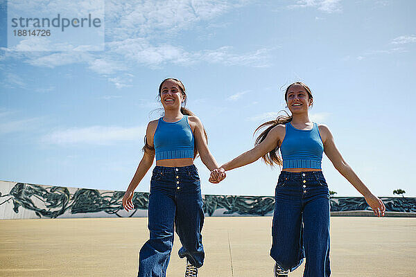 Happy girls holding hands and running in skateboard park