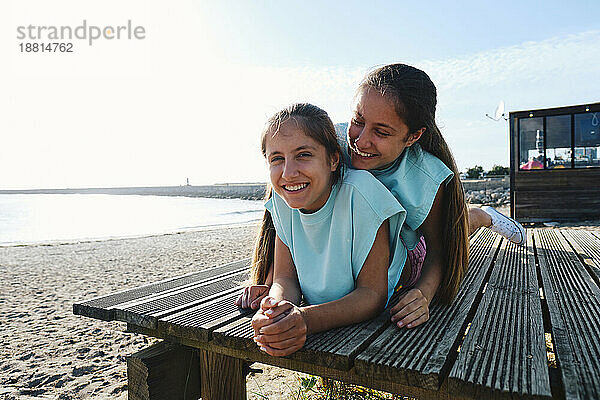 Glückliche Zwillingsschwestern  die Spaß daran haben  auf dem Steg am Strand zu liegen