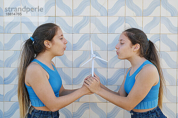 Zwillingsschwestern blasen vor der Wand auf ein Windturbinenmodell