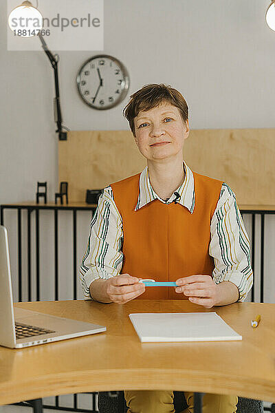 Lächelnde Frau sitzt im Klassenzimmer und blickt auf die Kamera  die den Online-Kurs aufzeichnet