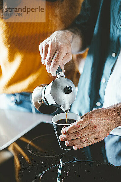 Mann gießt Kaffee in Tasse neben Keramikherd