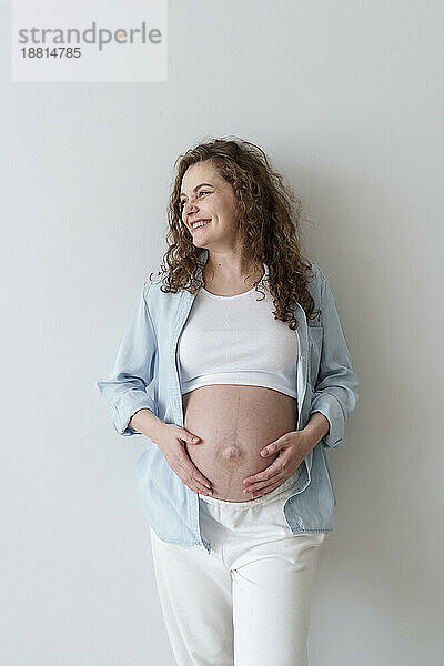 Smiling pregnant woman standing in front of wall