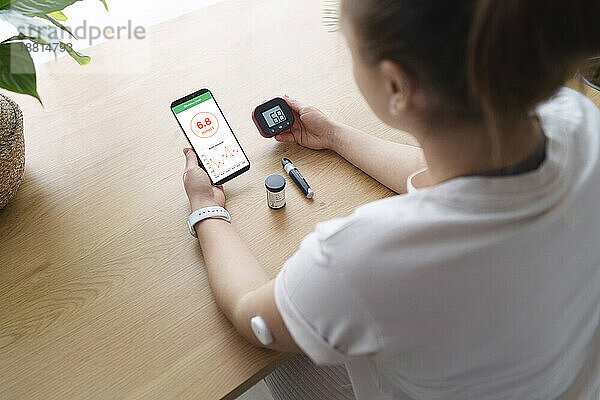Frau mit Diabetes synchronisiert Smartphone und Blutzuckermessgerät zu Hause