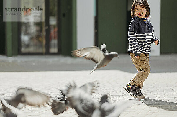 Fröhlicher Junge  der im Park mit Tauben spielt