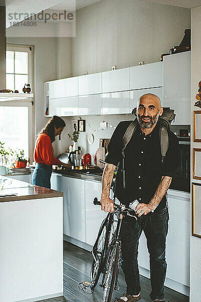 Reifer Mann steht mit Fahrrad in der heimischen Küche