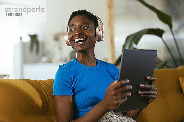 Fröhlicher junger Freiberufler mit Tablet-PC auf Sofa sitzend
