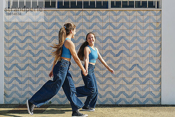Happy girls holding hands and running in front of wall
