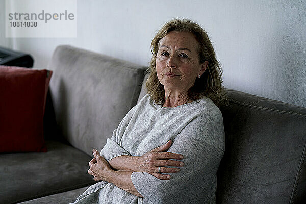 Ältere Frau sitzt mit verschränkten Armen zu Hause auf dem Sofa