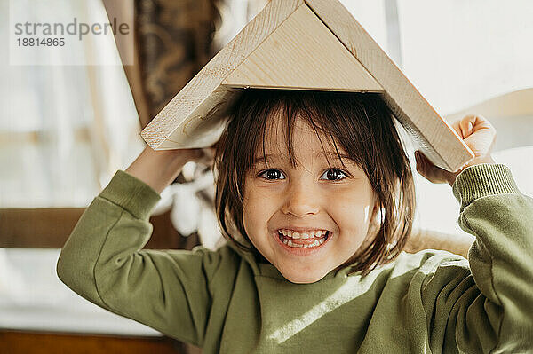 Lächelnder Junge hält zu Hause ein Vogelhaus über dem Kopf