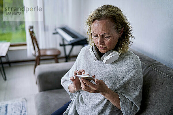 Ältere Frau benutzt Smartphone auf Sofa zu Hause