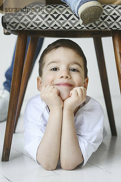 Lächelnder Junge stützt sich auf die Ellbogen unter dem Stuhl