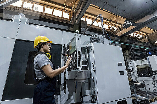 Wartungstechniker mit Schutzhelm und CNC-Maschinentastatur in einer modernen Fabrik